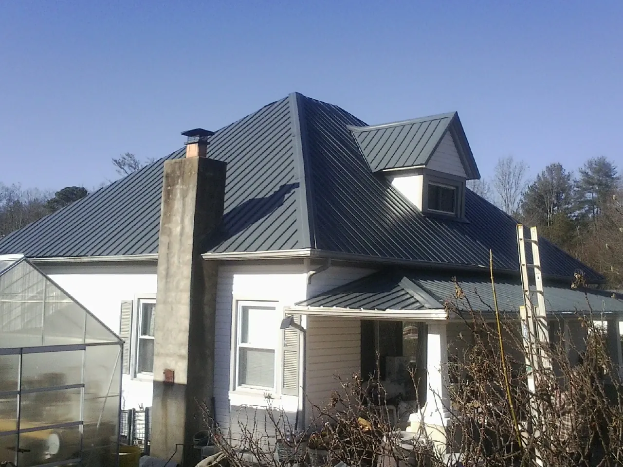 Dark blue standing seam metal roof on a white farmhouse with dormer — Slate & Tile Roof Repair by Roofing Brothers in Crater Lake