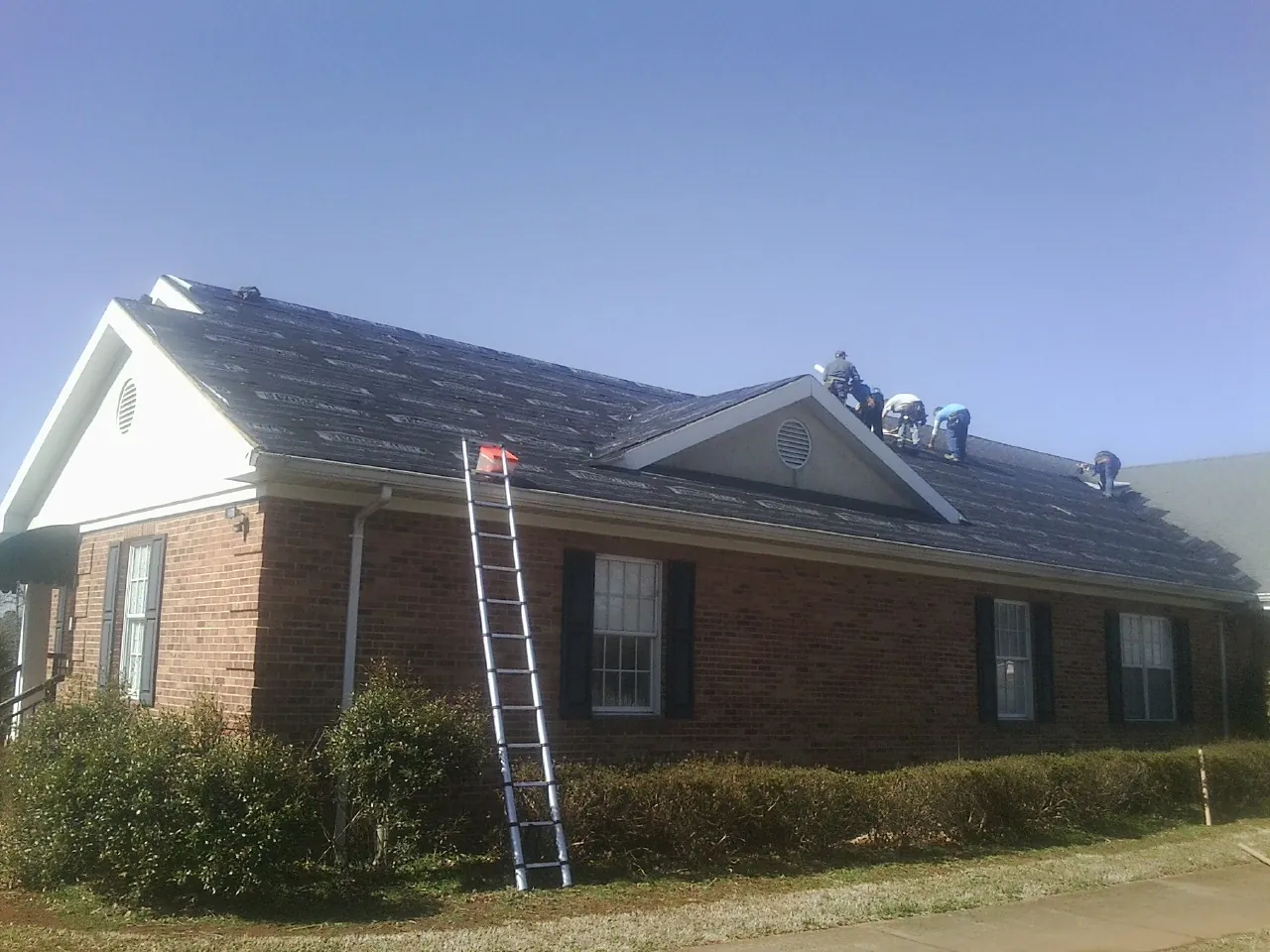 Crew tearing shingles off a brick ranch roof with a ladder set — Emergency Roof Repair work by our crew in Crater Lake