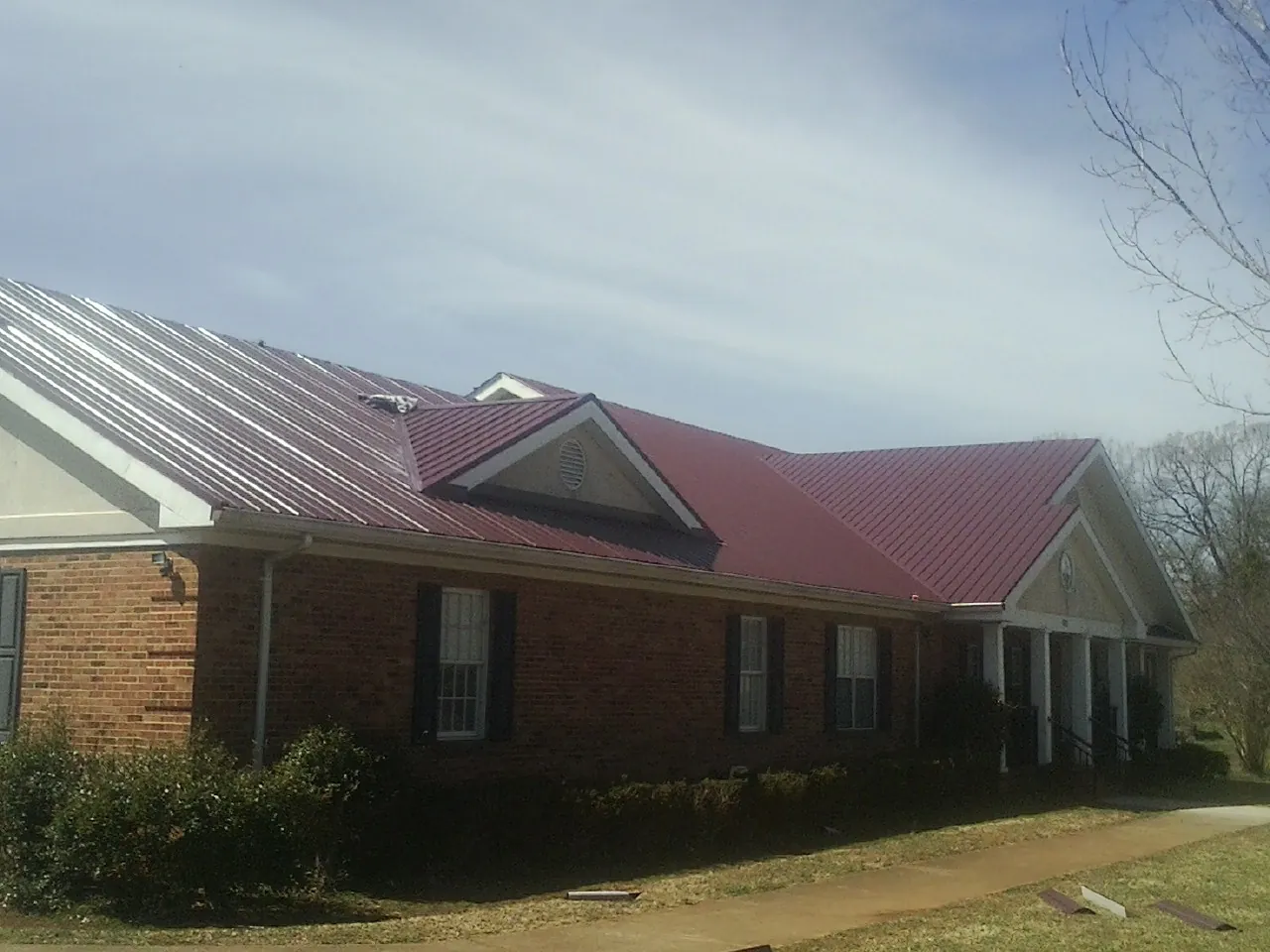 Red metal roof with gabled entries on a long brick building, from a Hail Damage Roof Repair job in Crater Lake