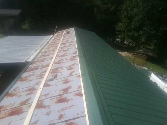 Old rusted panels beside newly installed green metal roofing — Wind Damage Roof Repair by Roofing Brothers in Crater Lake