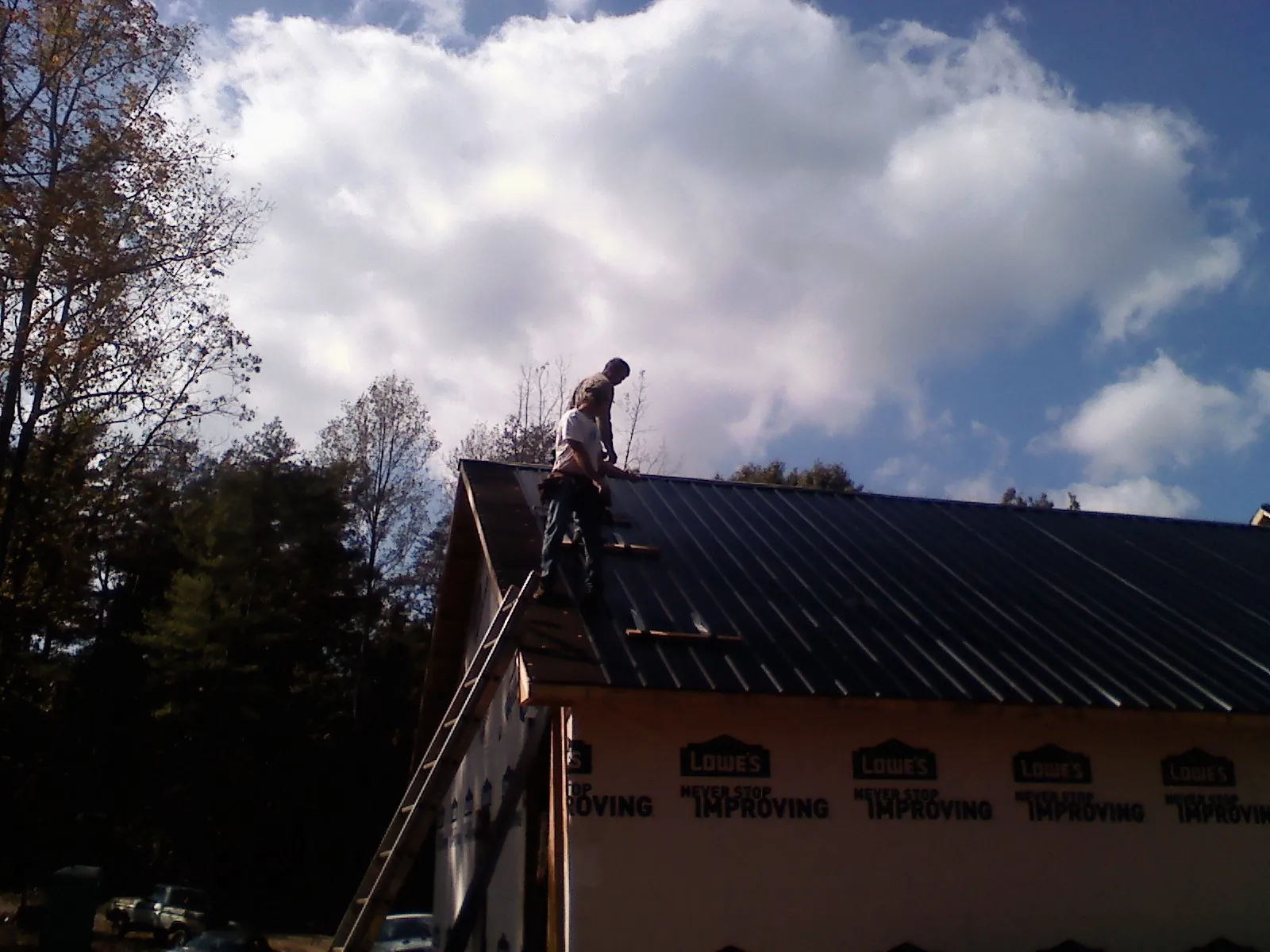 Roofer fastening dark metal panels high against a cloudy sky, from a Roof Inspection job in Crater Lake